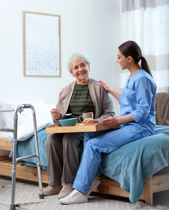 Caregiver assisting an elderly woman with a meal in a retirement home in Kanata, Ontario.