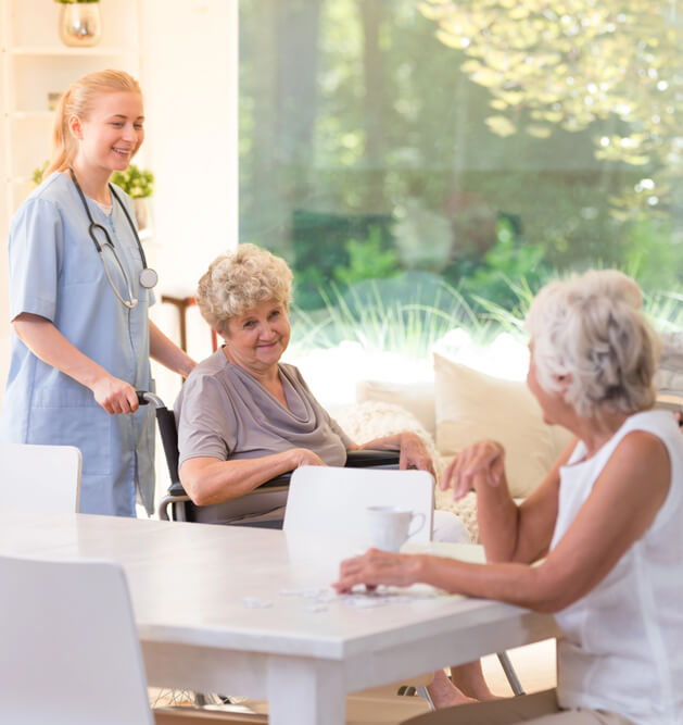 Caregiver assisting a resident while seniors socialize at a retirement home in Orléans, Ontario.